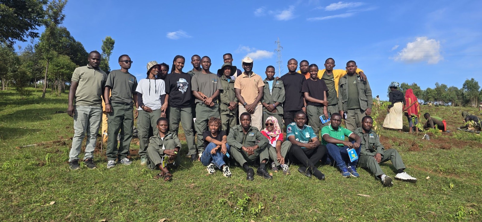 Yves Shema with a large tree-planting team seated and standing on a green hillside under a blue sky.